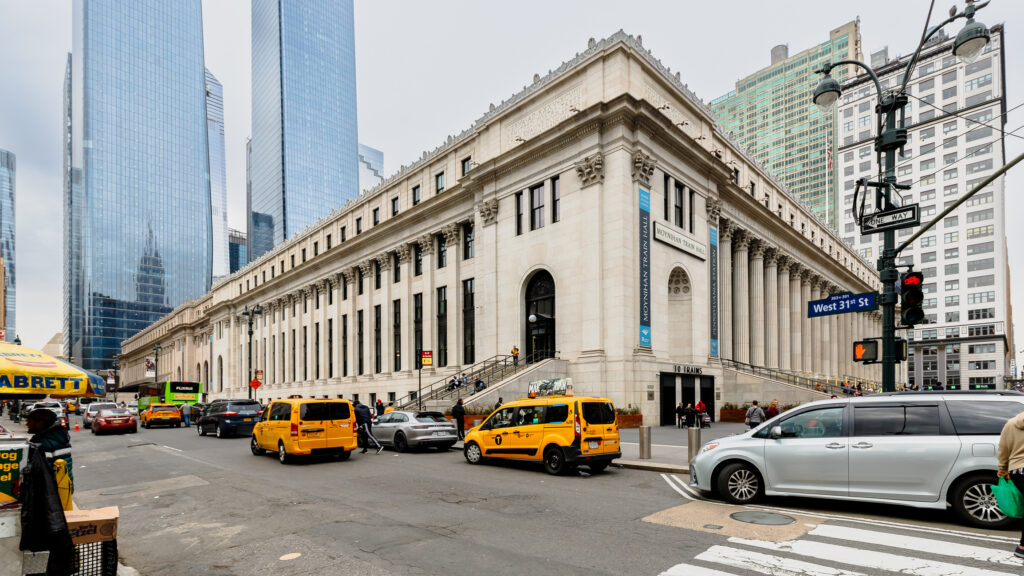 Moynihan Train Hall at Penn Station in New York City with yellow cabs and pedestrians on West 31st Street