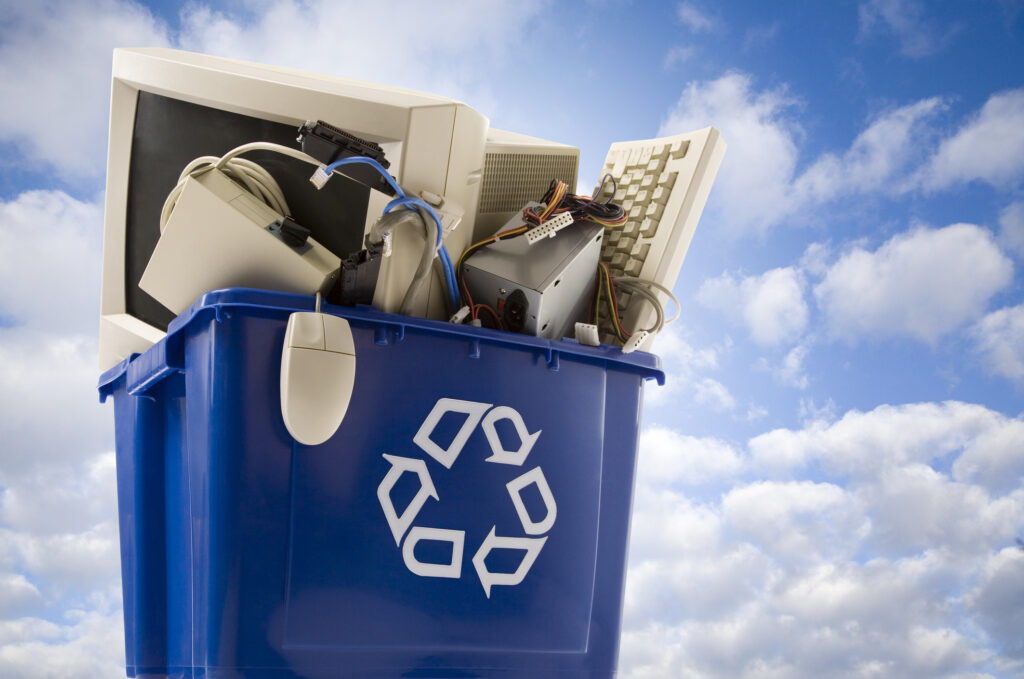 Blue recycling bin filled with old computer equipment under a bright sky, symbolizing responsible electronics recycling