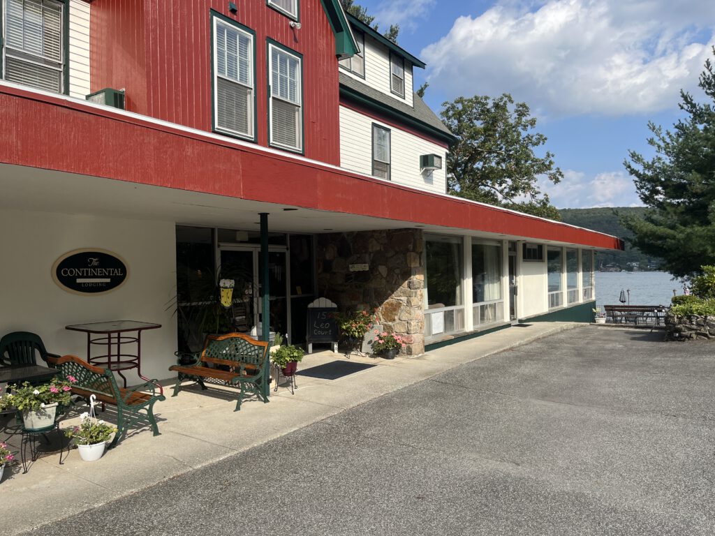 Exterior view of The Continental Hotel in Greenwood Lake, New York, with lake and patio seating visible in the background.