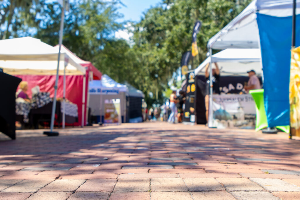 View of vendor tents and booths at a sunny outdoor street fair, with colorful canopies lining a brick walkway