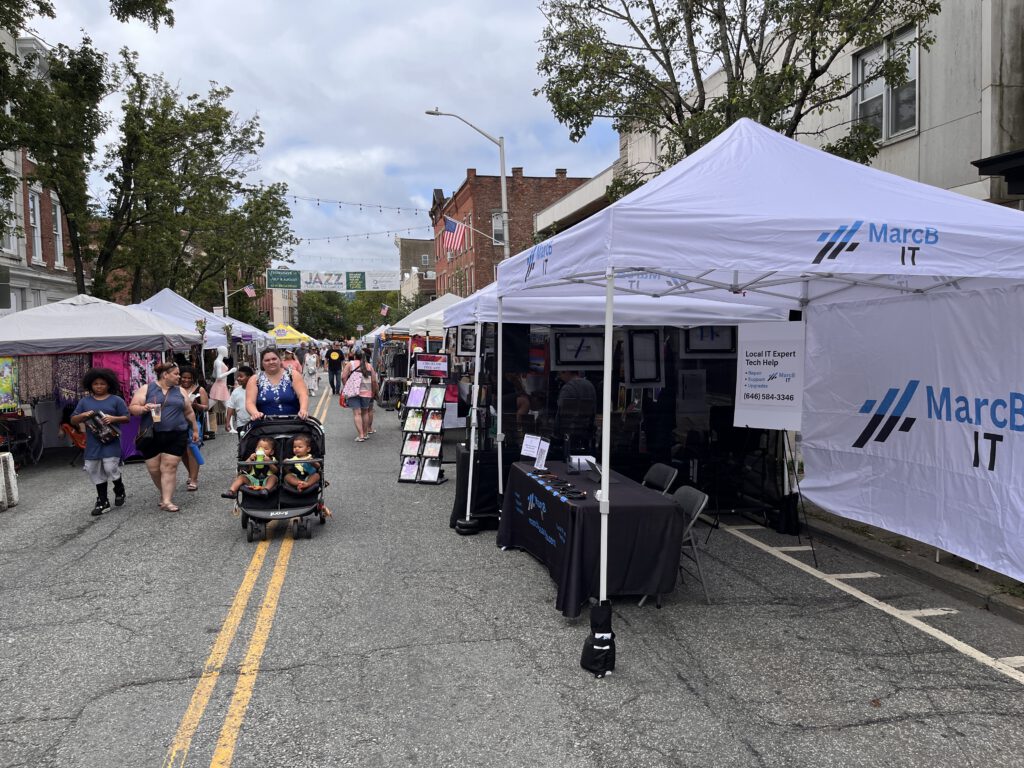 MarcB IT booth at the Nyack Street Fair with attendees walking by on North Broadway.