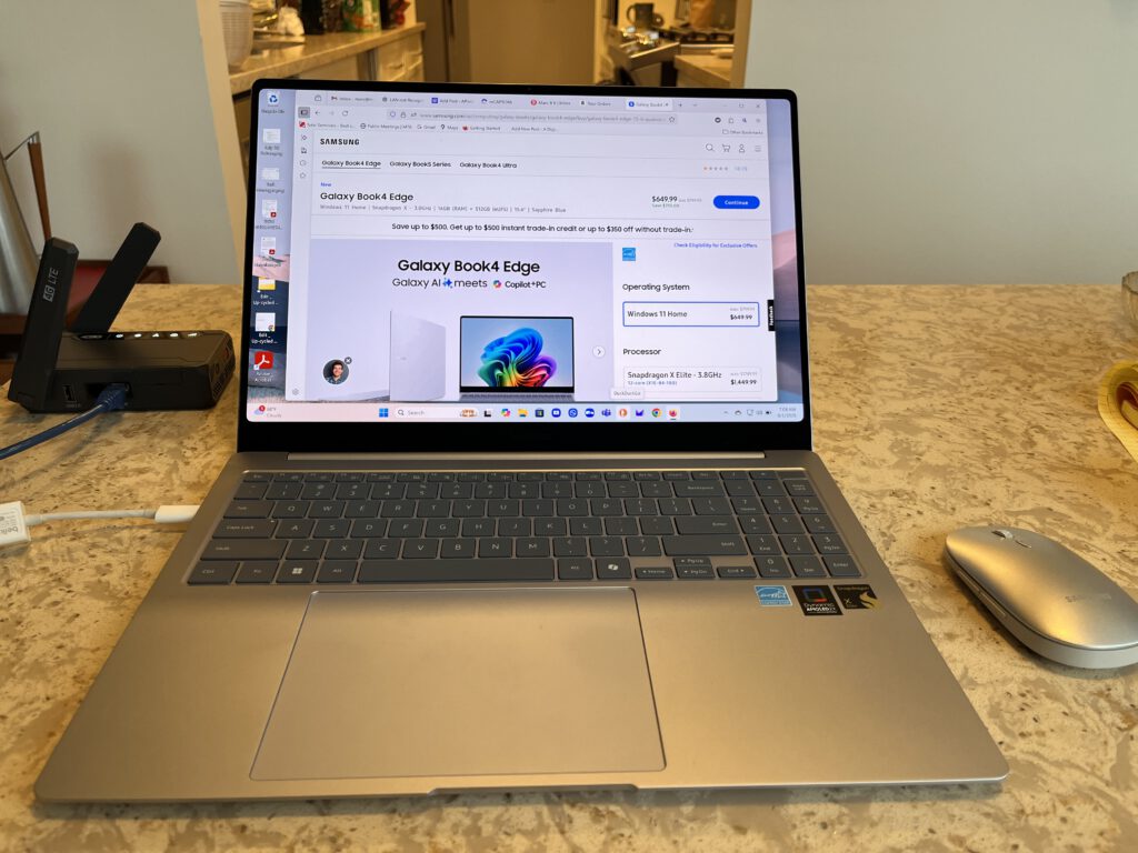 Samsung Galaxy Book4 Edge laptop powered on after repair, shown on a kitchen counter next to a Logitech mouse and Verizon CSG mobile hotspot