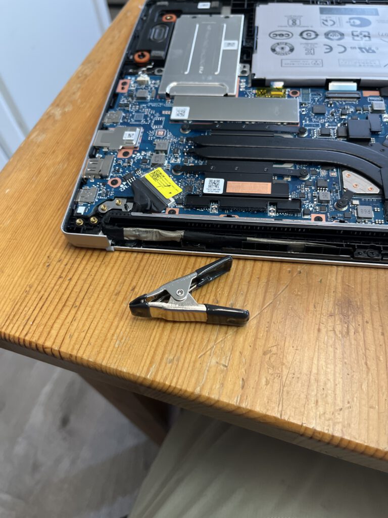 Open Samsung laptop showing internal components during hinge repair attempt with clamp